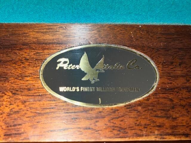 Pool table with green felt and ornate wooden detailing, set on a magenta rug.