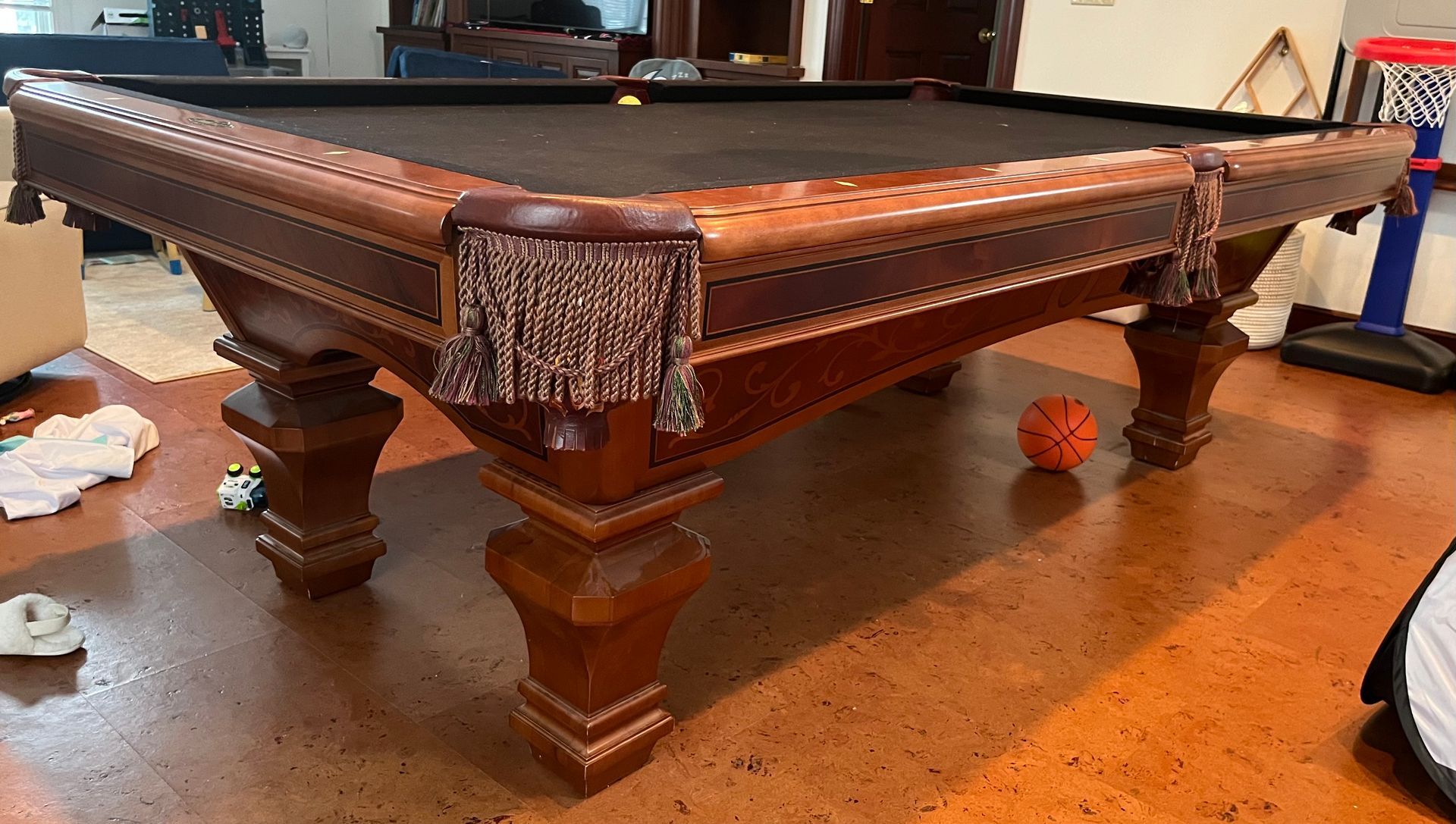 Pool table with dark felt, brown wood, and decorative tassels. A basketball sits nearby.