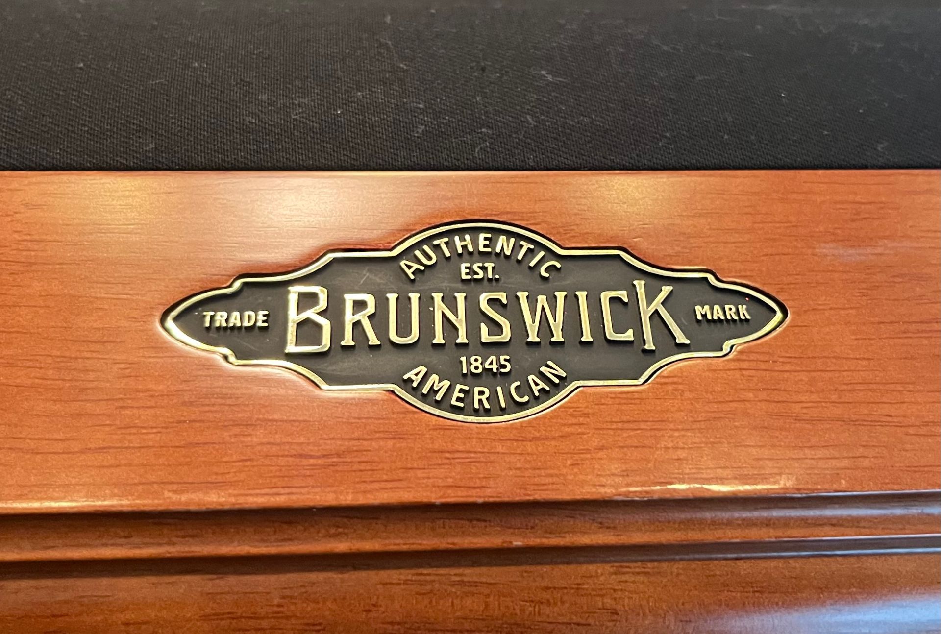 Brunswick logo plaque on wooden surface. Brass-colored lettering on a dark background. 