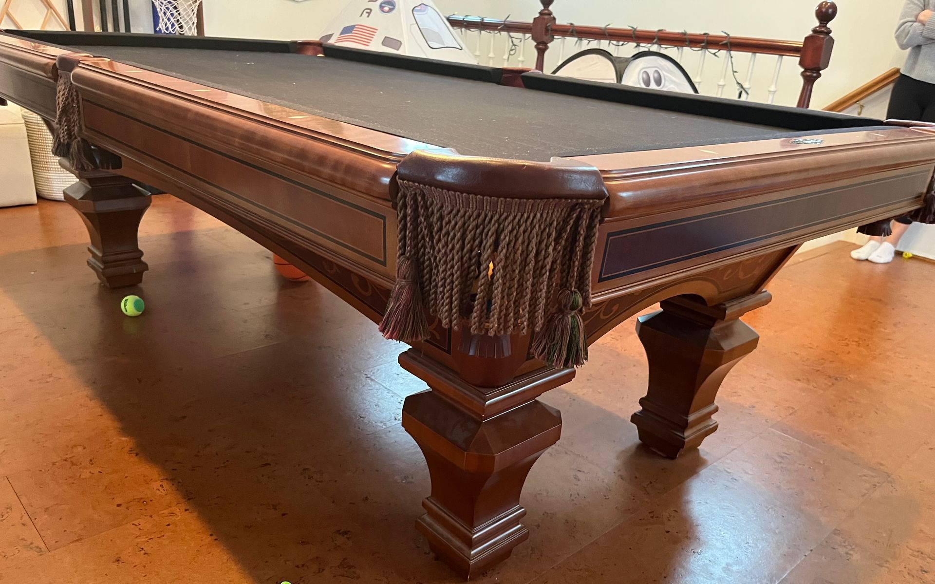Brown wooden pool table with dark felt, tassels, and a green ball.