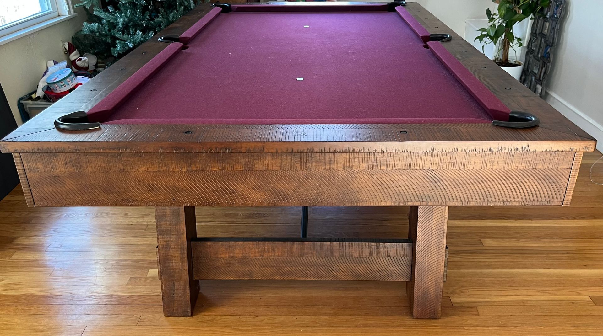 Wooden pool table with maroon felt and dark brown trim, in a room with hardwood floors.