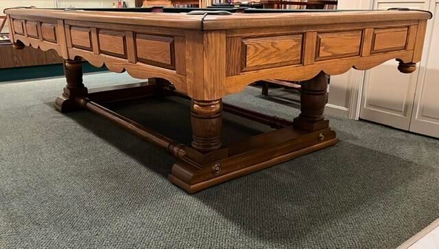 Large wooden pool table with carved legs on a carpeted floor in a room.