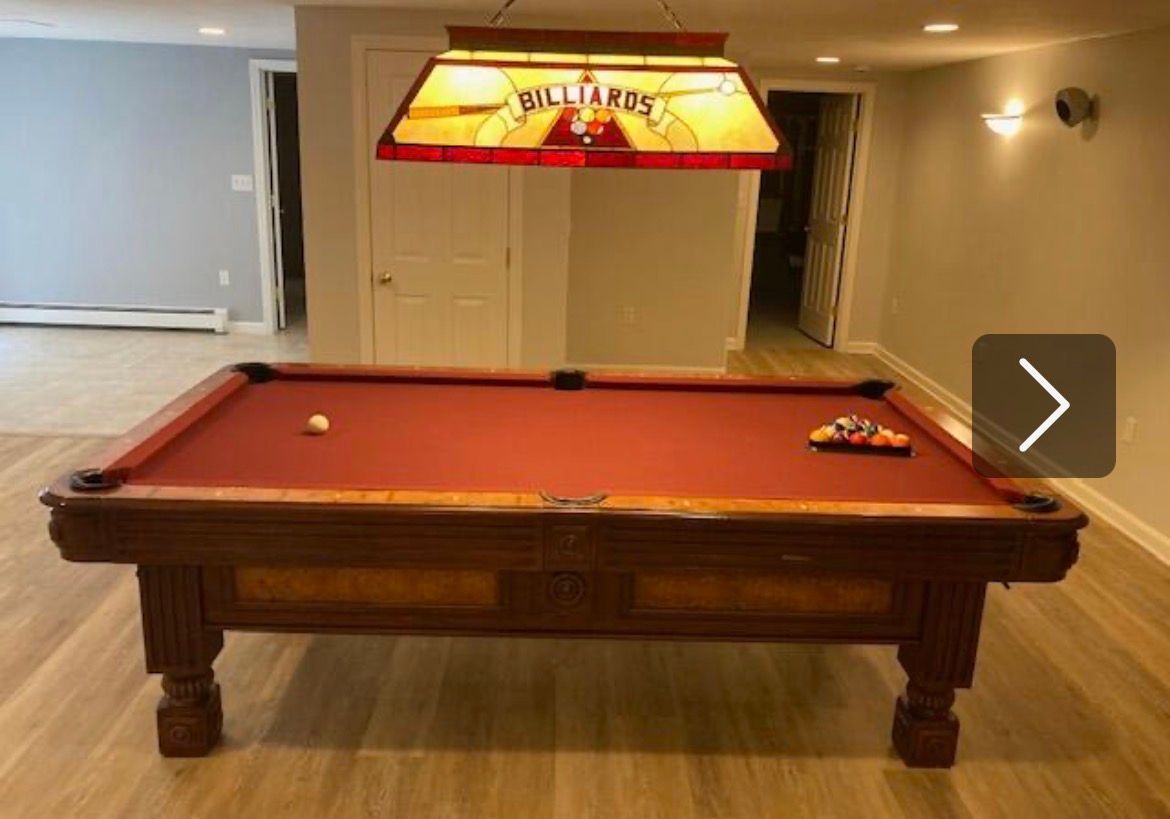 Billiards table under a hanging lamp in a carpeted basement rec room
