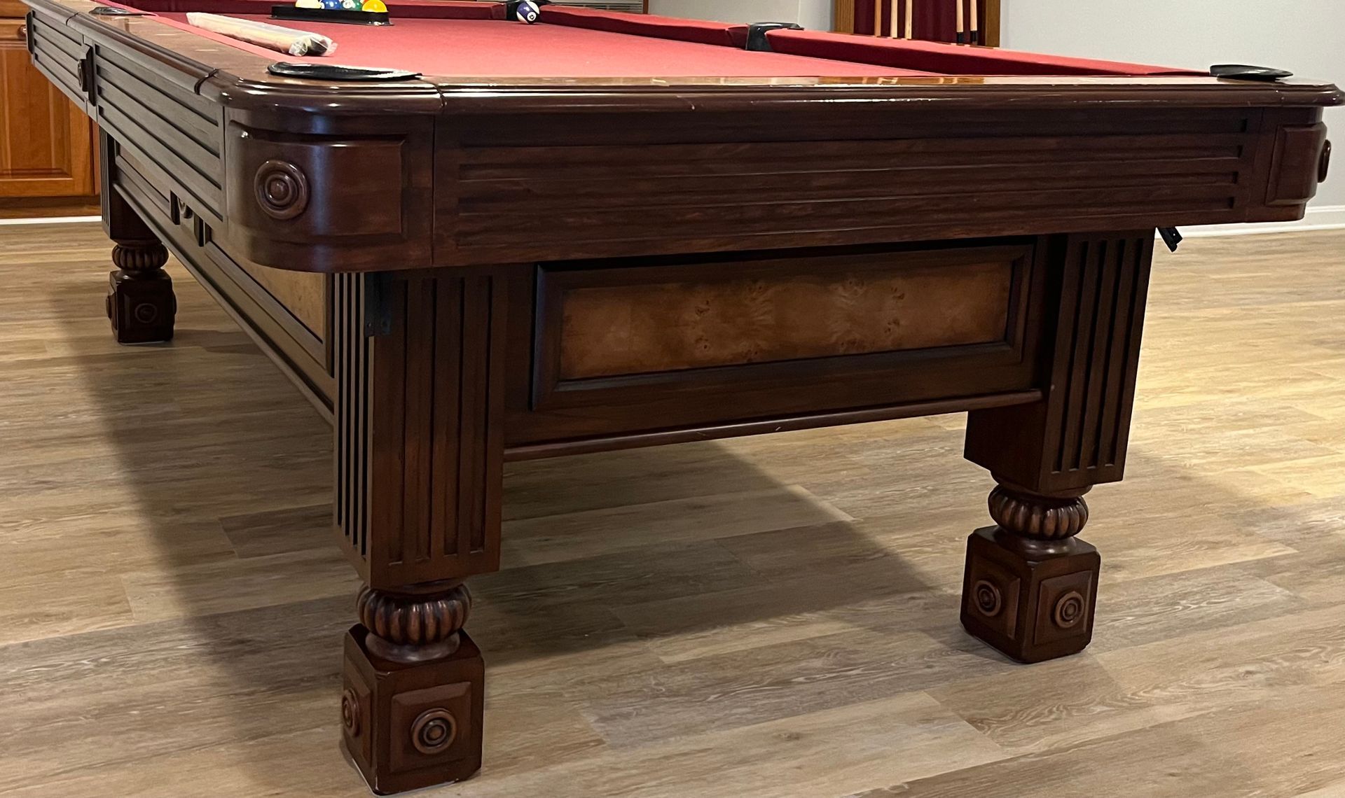 Dark wooden pool table with red felt in a game room on a light wood floor