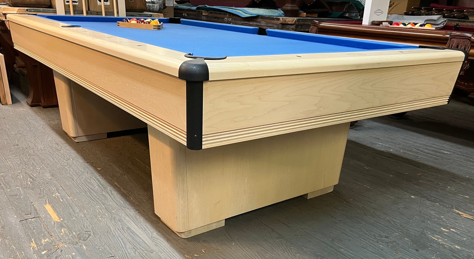 Pool table with blue felt, light colored wood frame, and hardwood floor.