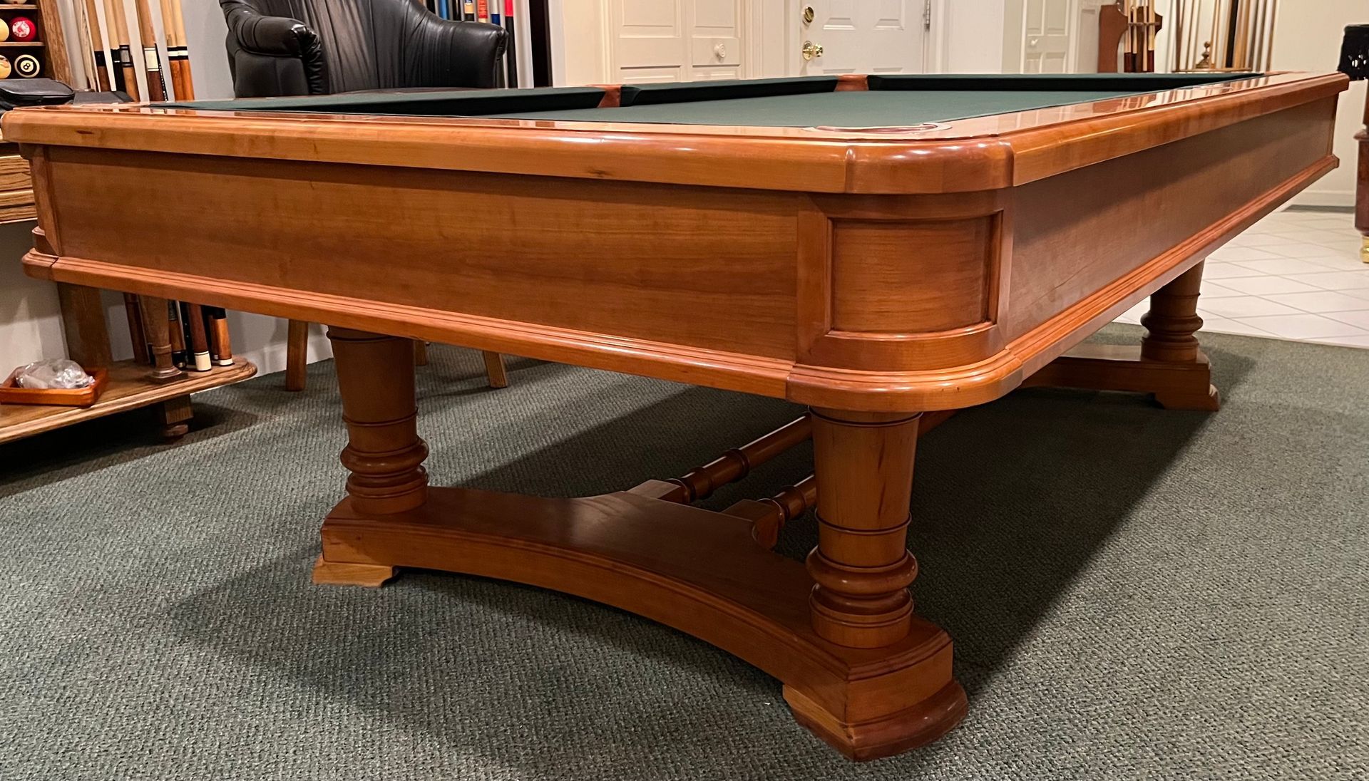 Wooden pool table with a black felt surface, set in a room with a concrete floor.