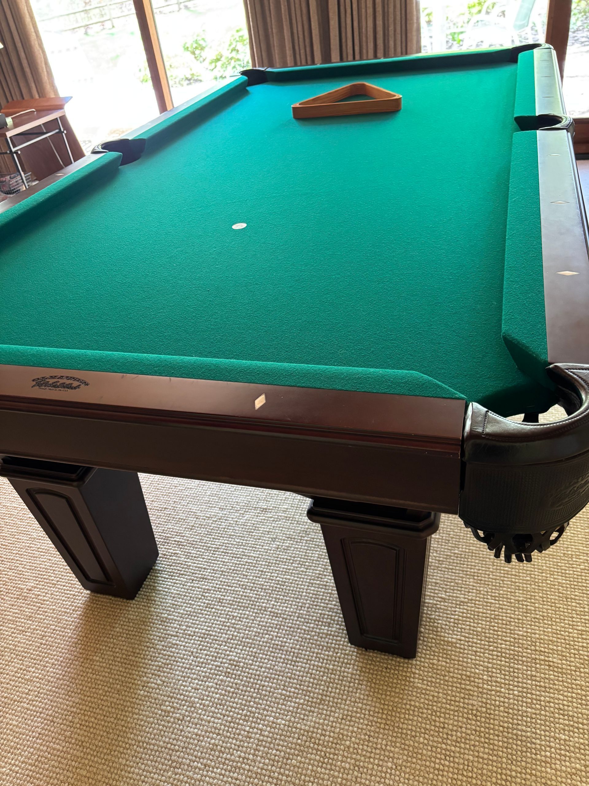Green pool table indoors with a billiard triangle rack near the far end.
