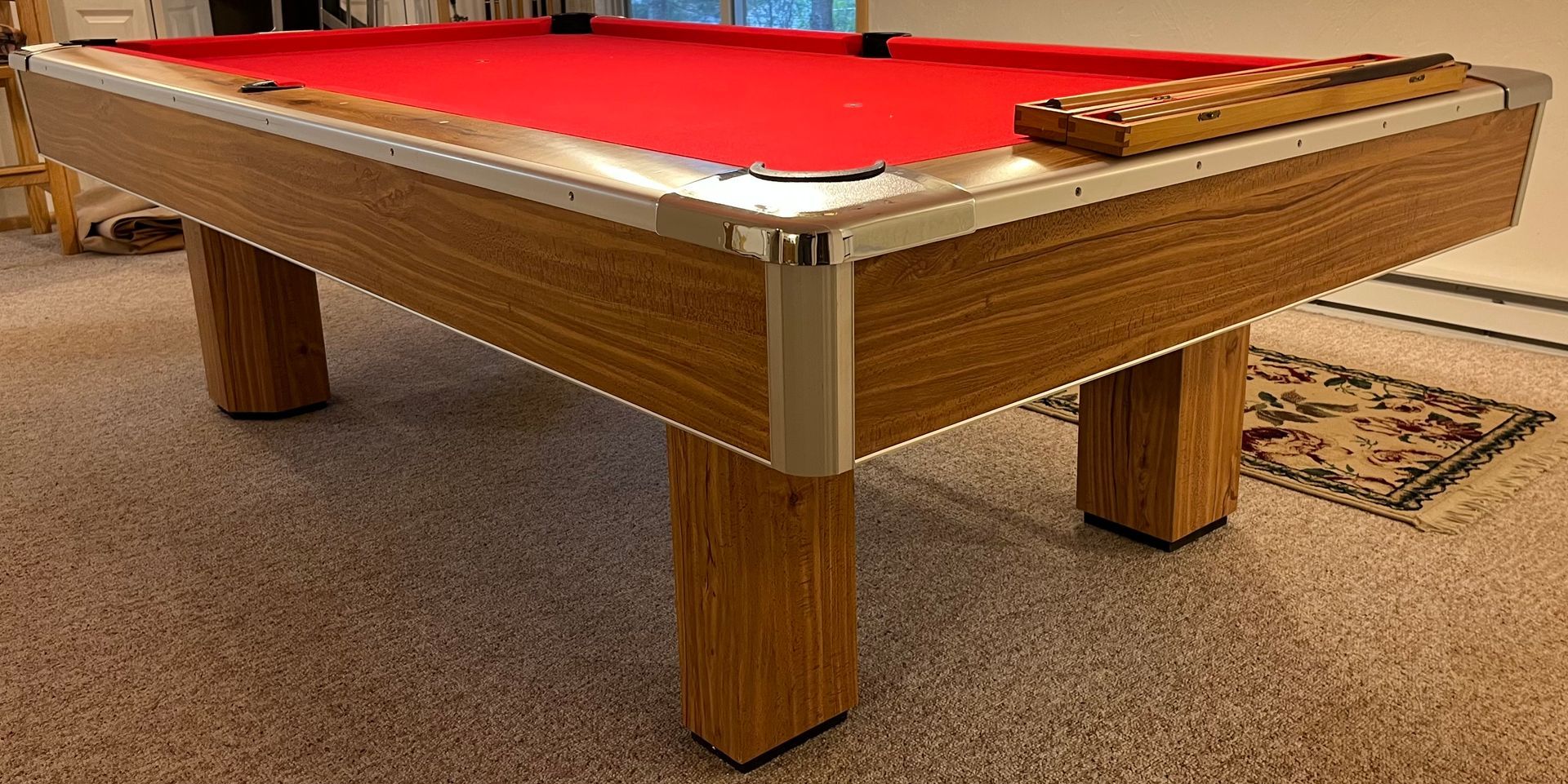 Pool table with red felt and wooden legs on a carpeted floor.