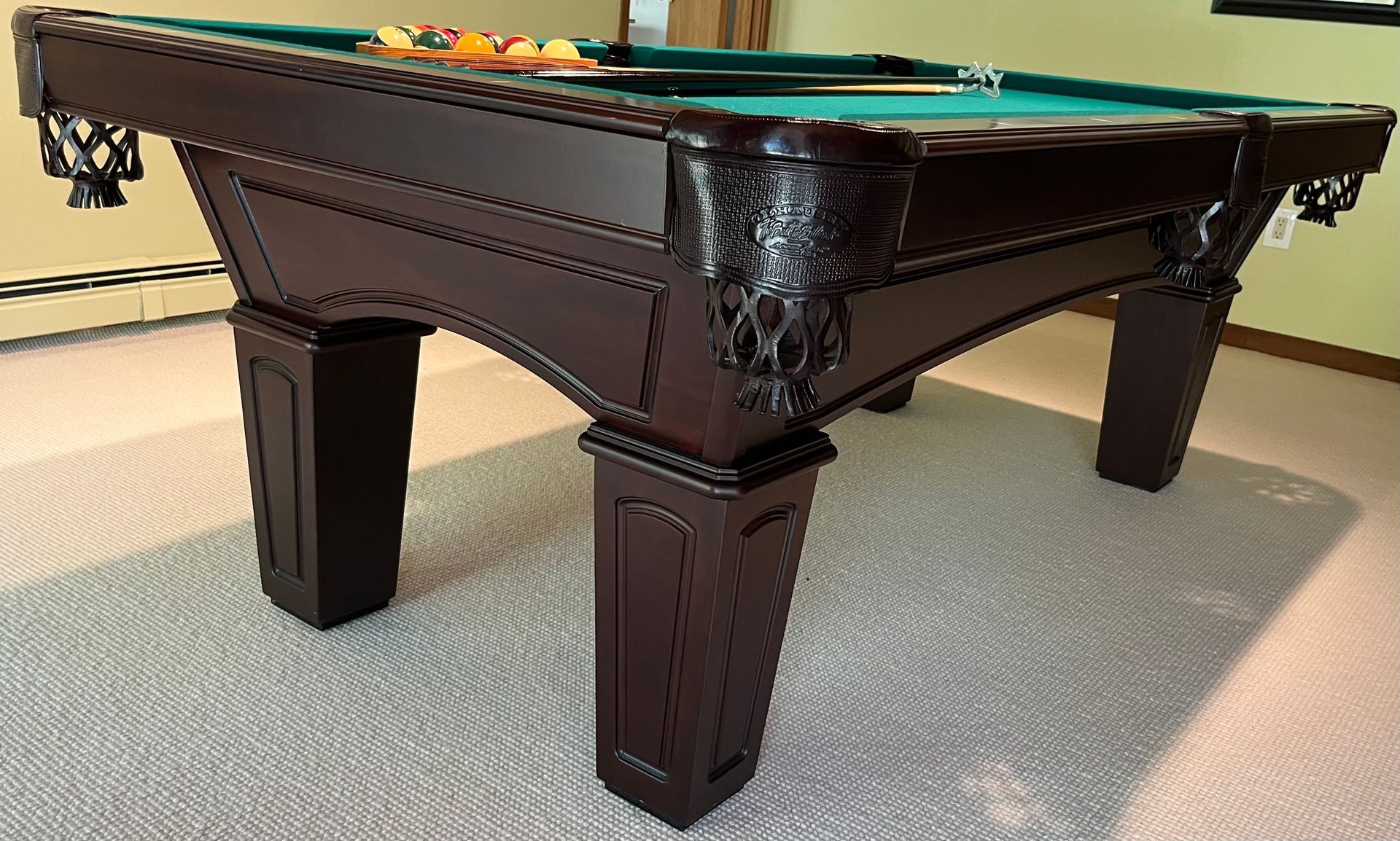 Dark brown carved pool table with green felt on a carpeted floor