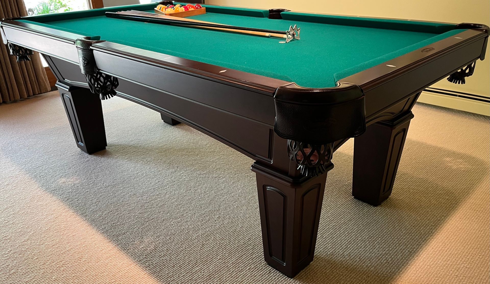 Pool table with green felt and cue sticks in a carpeted game room