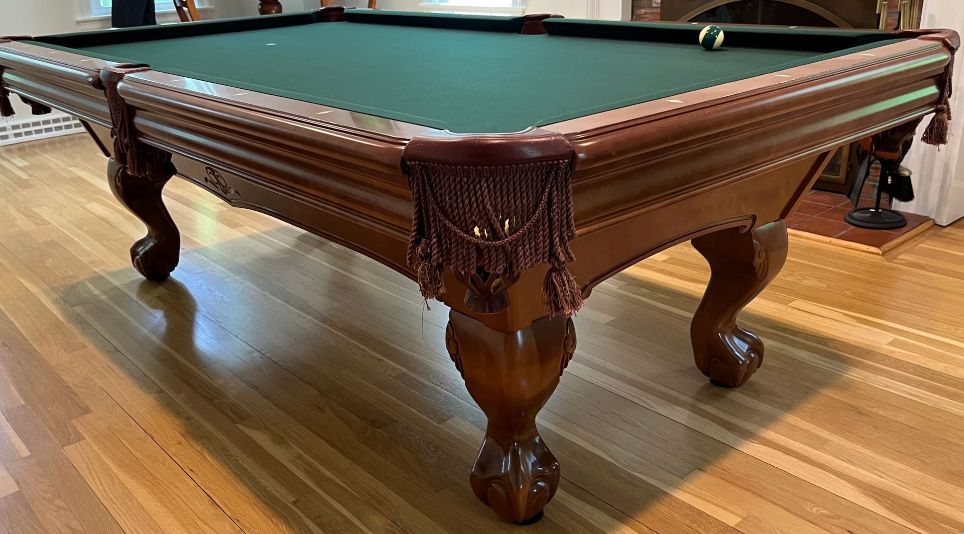 Wooden pool table with green felt and ornate carved legs in a room with hardwood floors