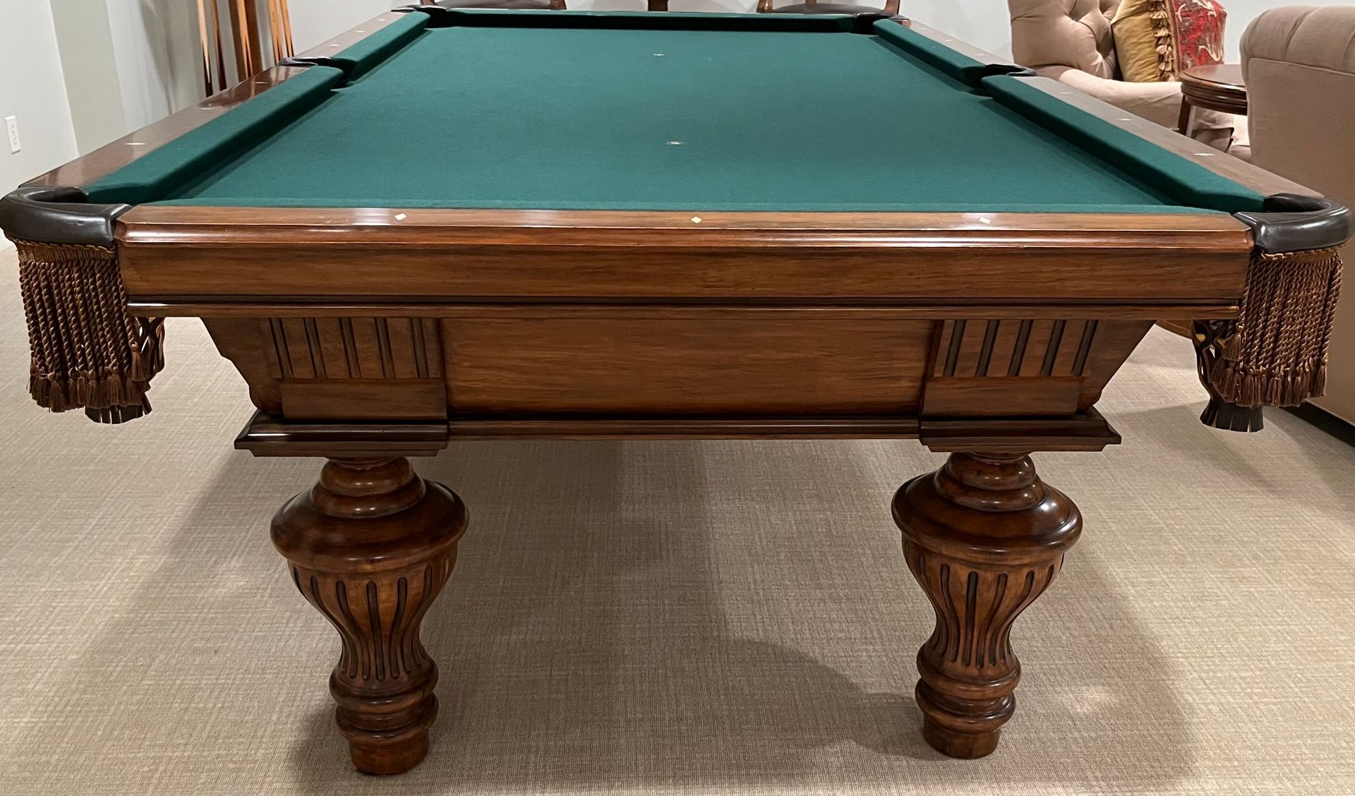 Wooden pool table with green felt, ornate legs, in a carpeted room