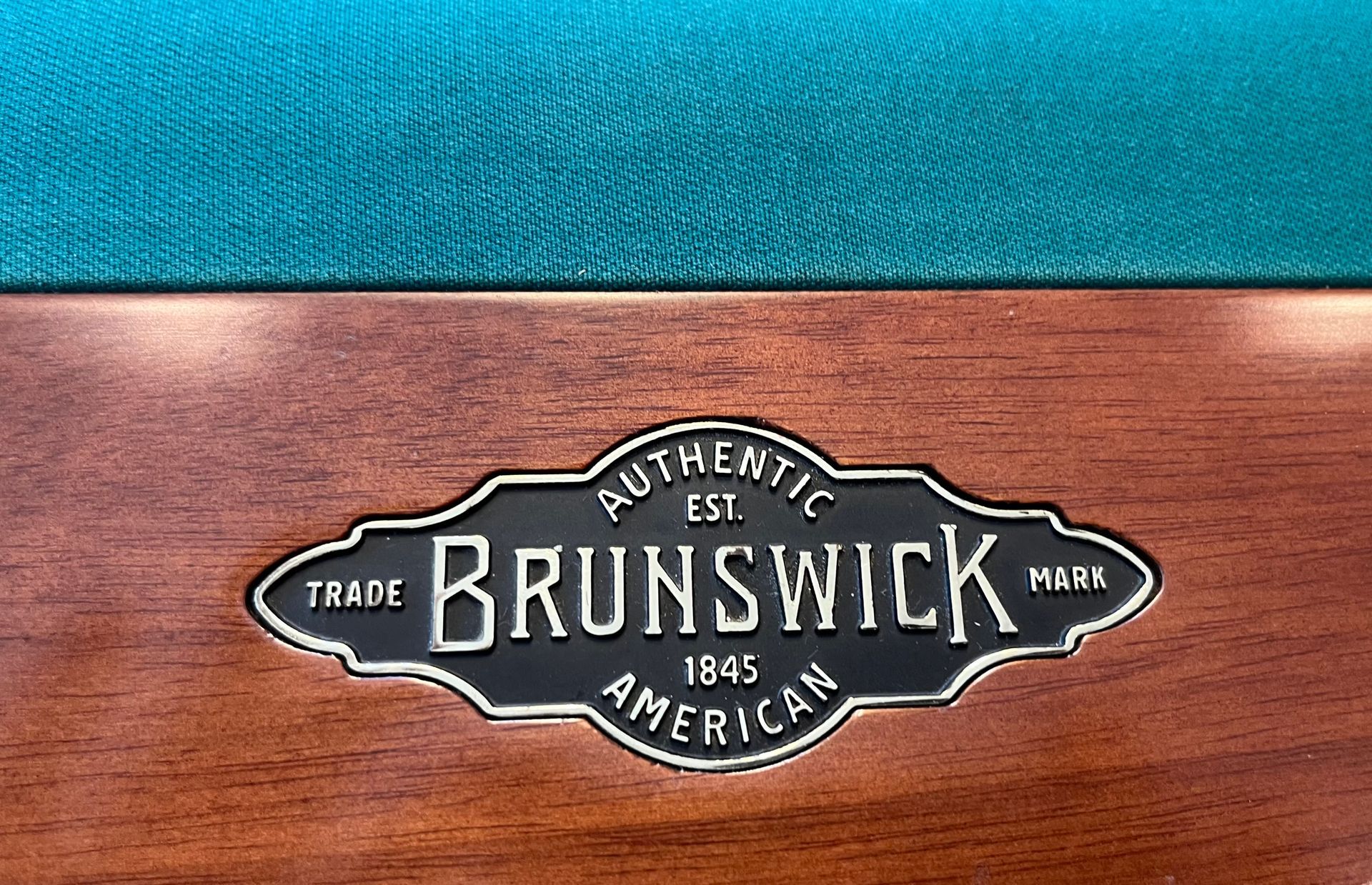 Brunswick logo on a polished wood panel with teal felt above