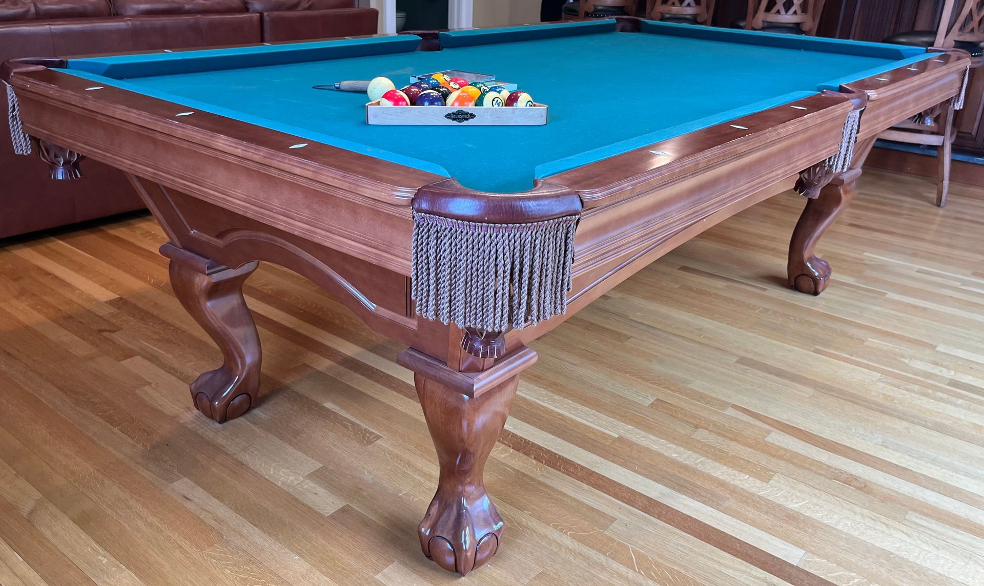 Blue-felt pool table with balls and a fringed pocket in a wooden room