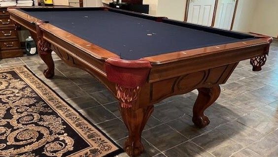 Pool table with dark blue felt, ornate wood frame, and carpet in a room.