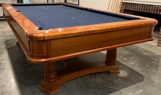 Wooden pool table with blue felt, in a room with a brick fireplace.