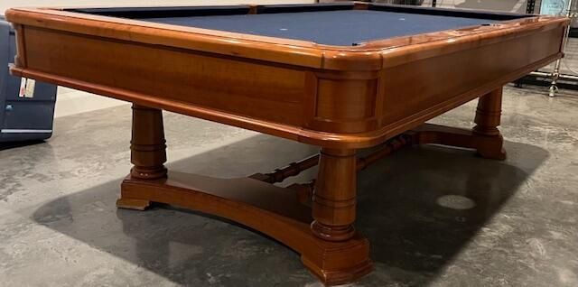 Wooden pool table with blue felt, in a room.