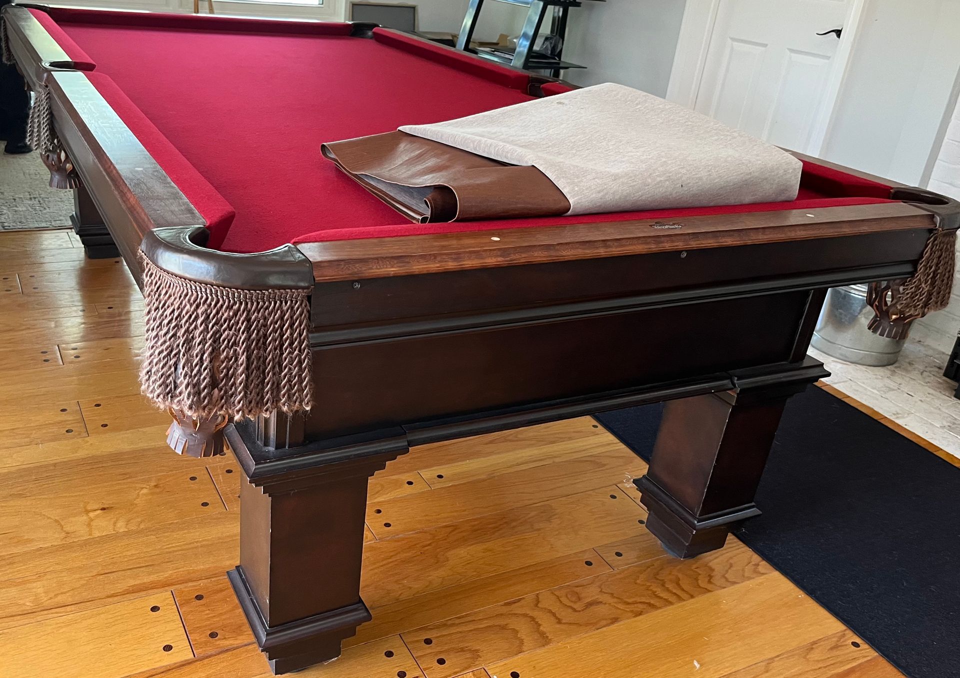 Pool table with red felt, brown wood, and fringed pockets in a room with wood floors.