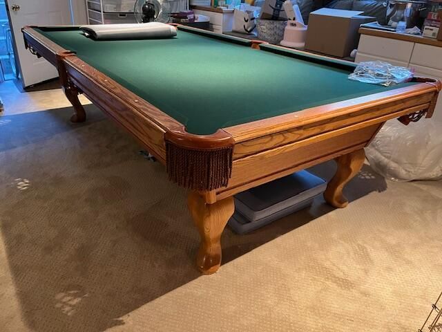 A wooden pool table with green felt, fringed pockets