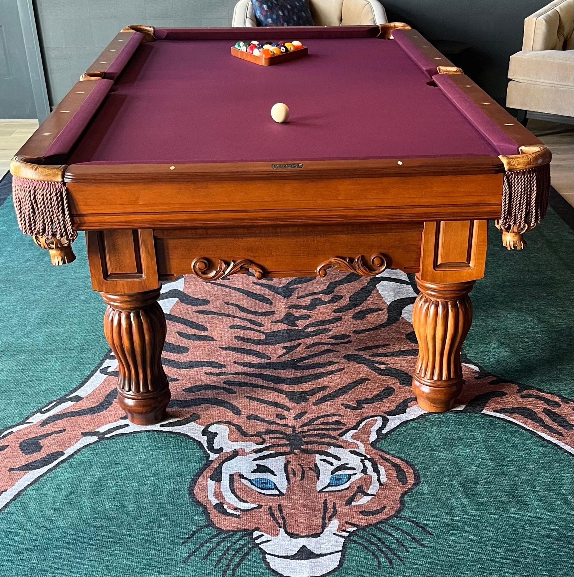 Pool table with burgundy felt and a tiger rug.