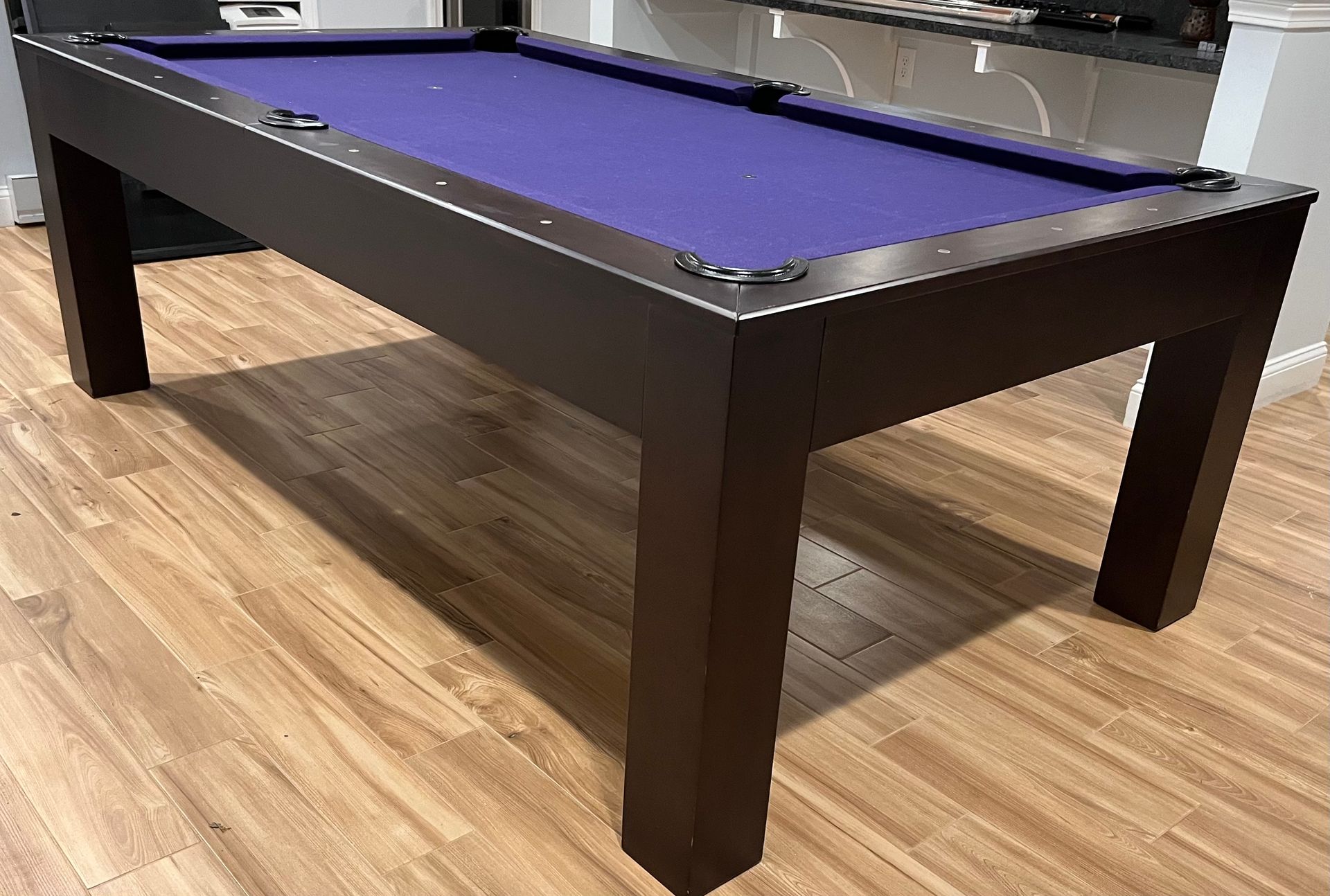 Dark brown pool table with purple felt, on wood floor.
