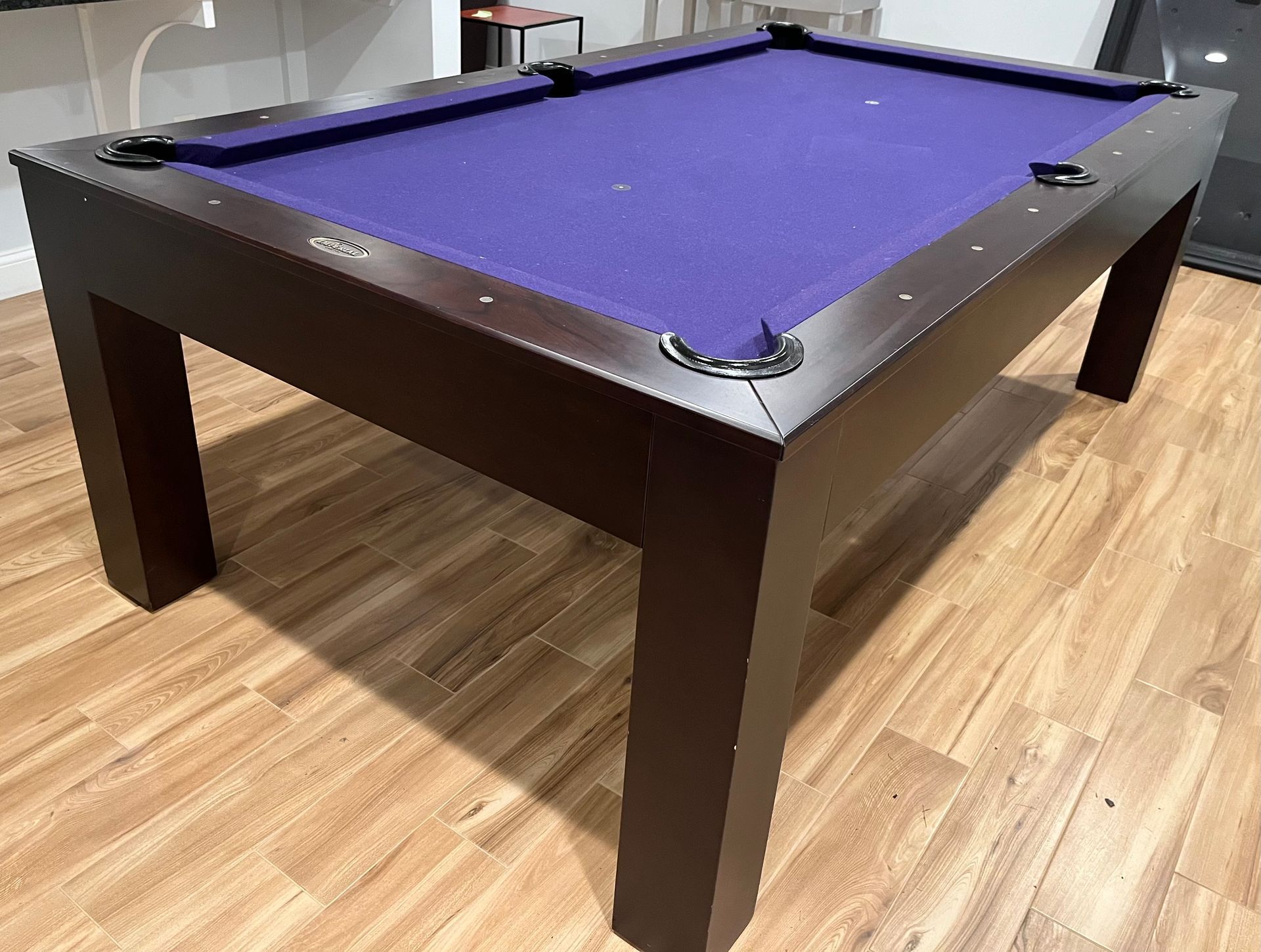A dark brown pool table with purple felt sits on a wood floor in a room.