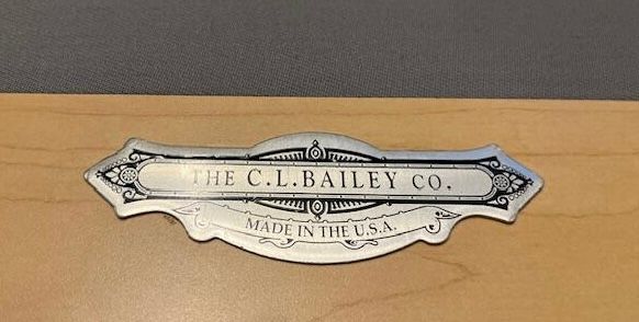 Silver plate, “THE C.L. BAILEY CO. MADE IN THE U.S.A.” mounted on light wood.