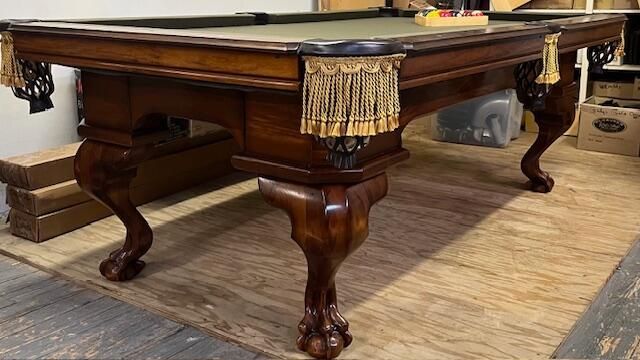 An antique-style wooden pool table with carved claw-and-ball feet and decorative tasseled pockets in a room.