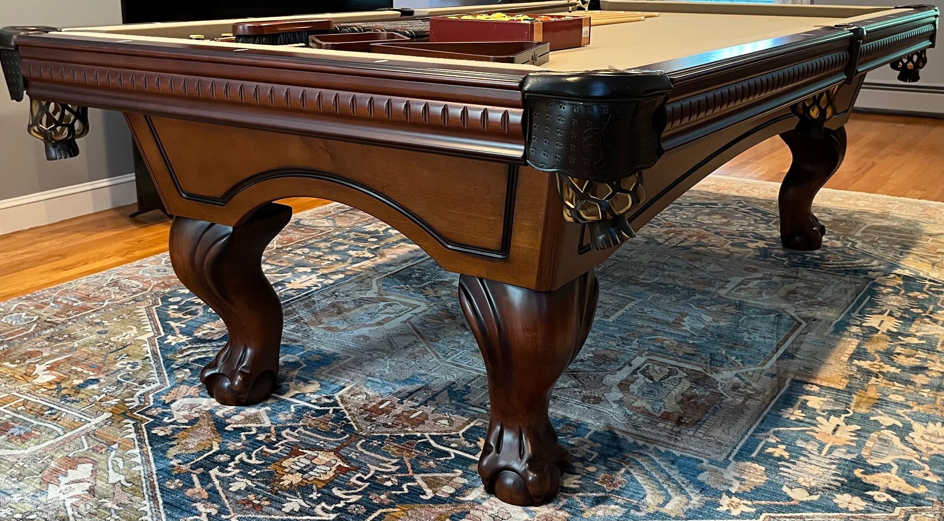 Ornate wooden billiards table with carved legs and leather corner pockets on a patterned rug