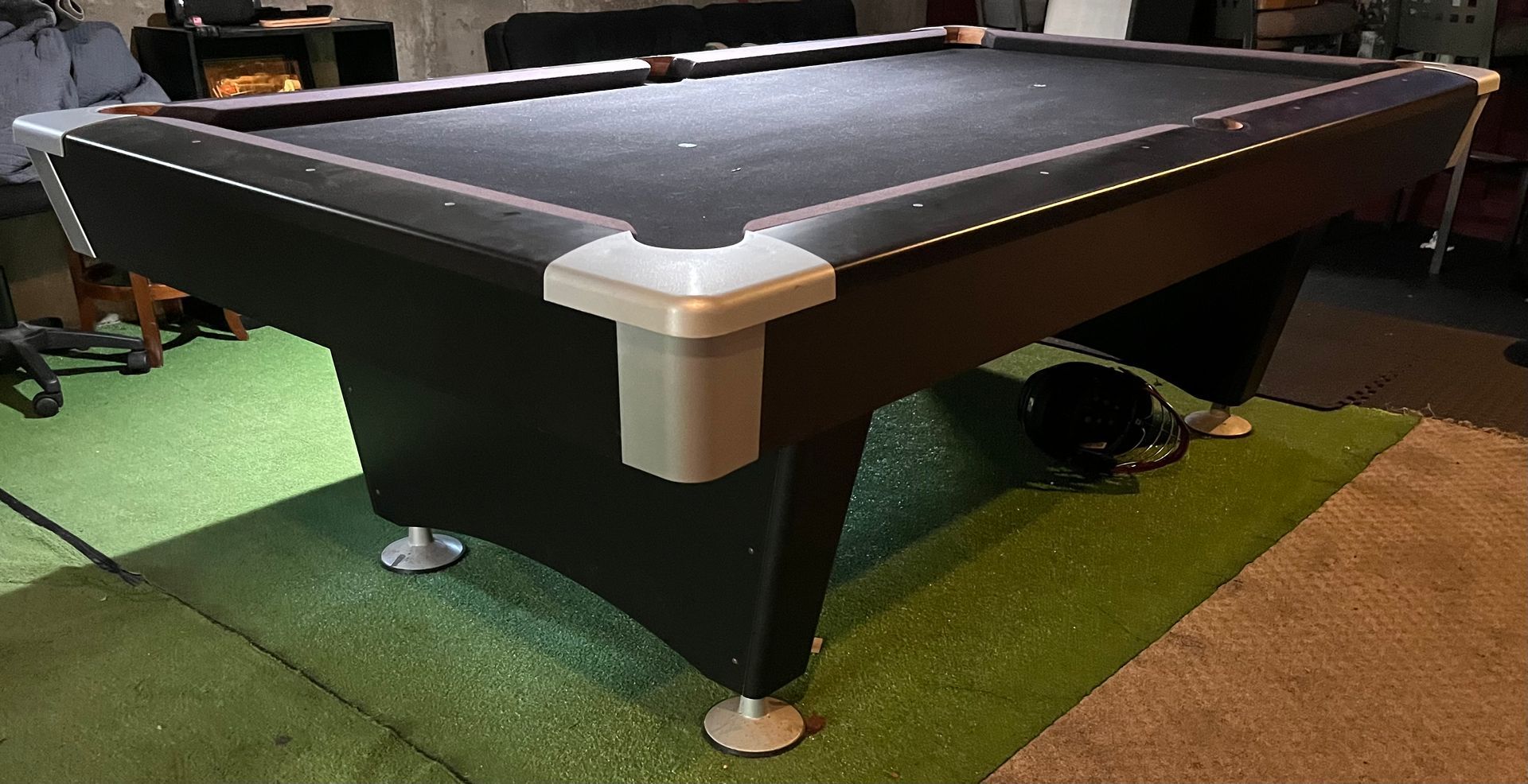 Black pool table on green carpet in an indoor game room