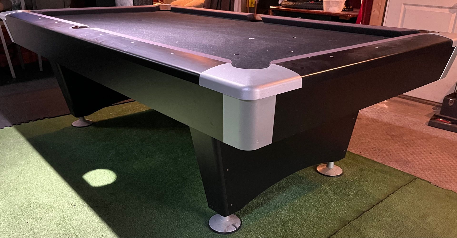 Pool table on green carpet with black felt and silver corner trim in a dim room