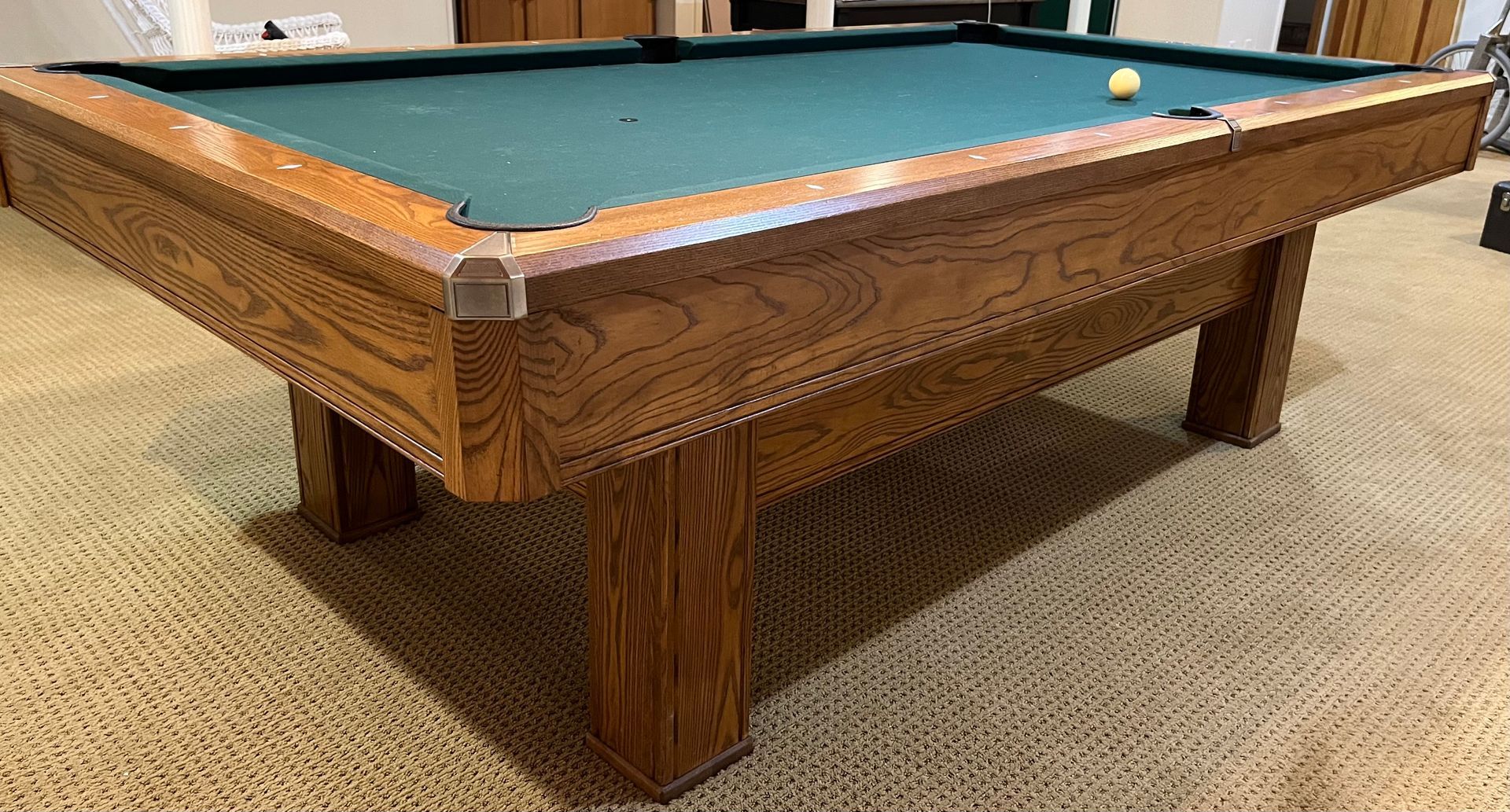 Wooden pool table with blue felt in a carpeted room, a cue ball near the corner pocket.