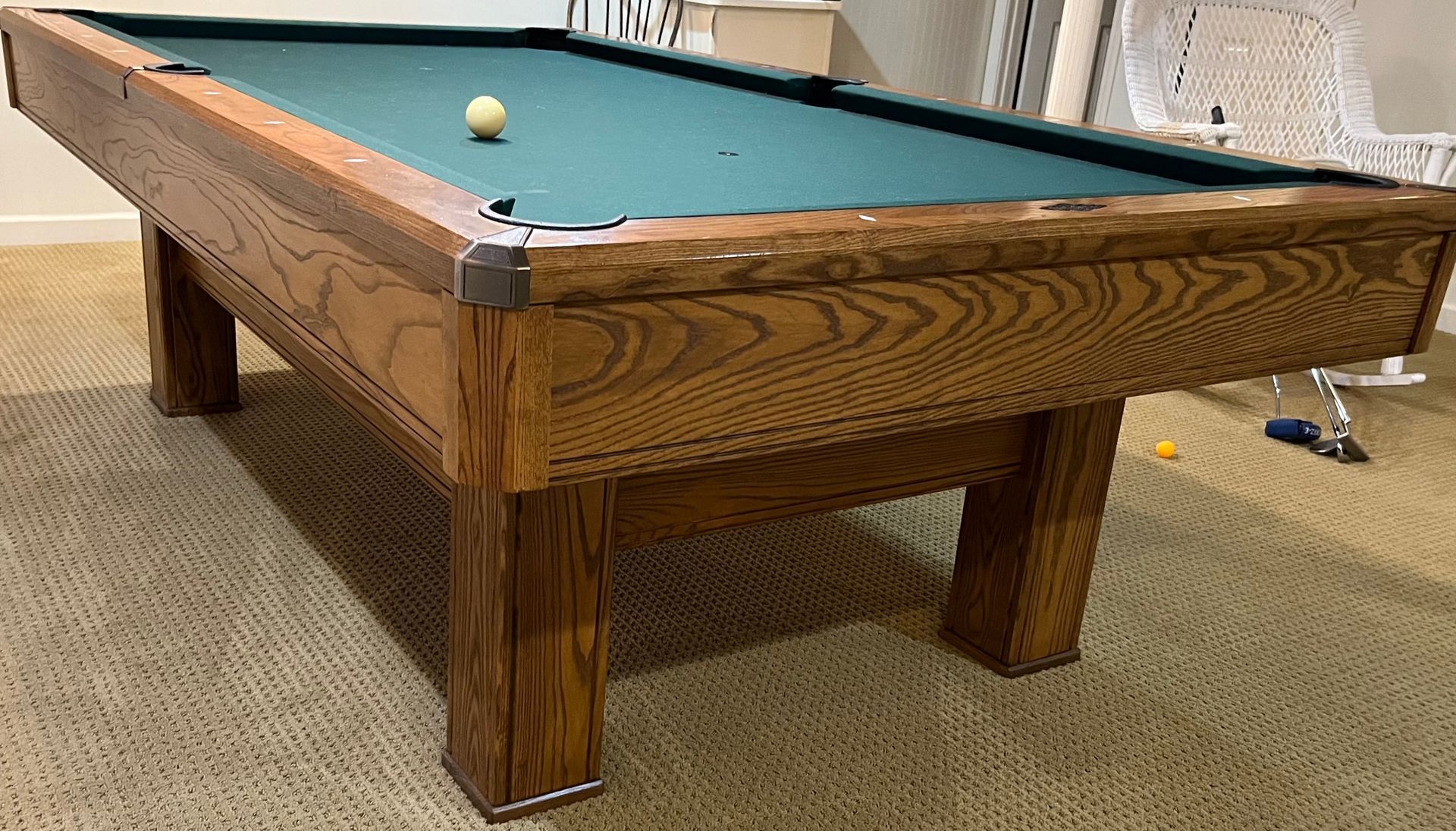 Wooden pool table with green felt and scattered balls in a carpeted room