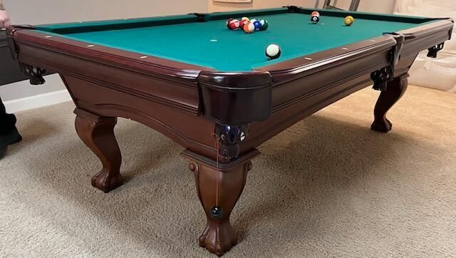 Wooden pool table with green felt and scattered billiard balls in a carpeted room