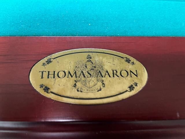 Oval Thomas Aaron nameplate on a polished wooden surface, with a turquoise background.
