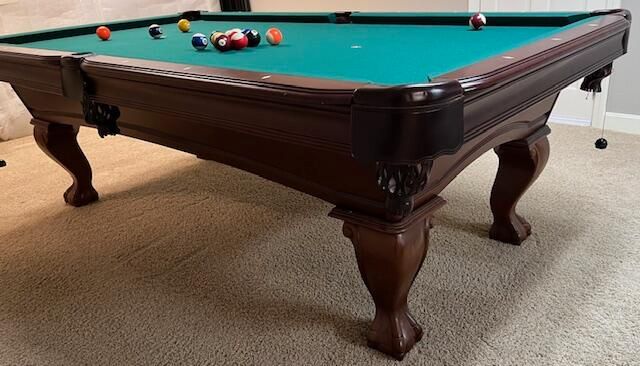 Pool table with green felt and scattered balls in a carpeted room