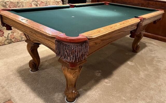 Wooden pool table with green felt and carved legs in a room with floral wallpaper.