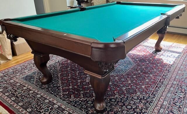 Brown pool table with green felt on a patterned rug in a room