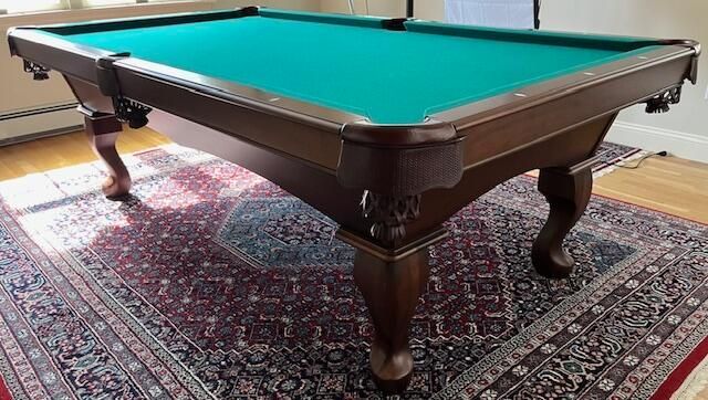Pool table with green felt on a patterned rug in a bright room