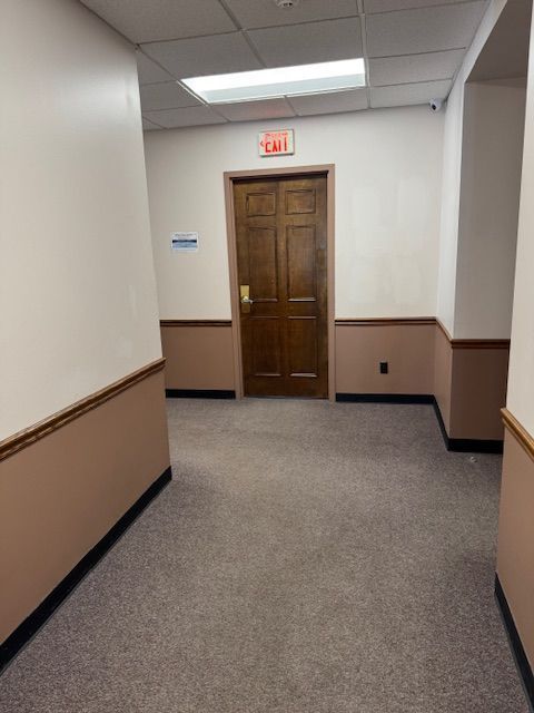 A hallway with a wooden door and a red exit sign
