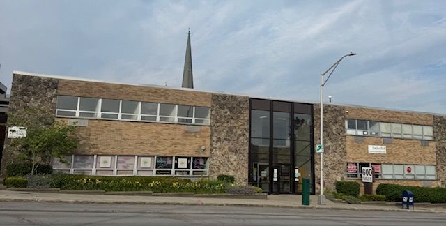A large brick building with a steeple on top of it is on the corner of a street.