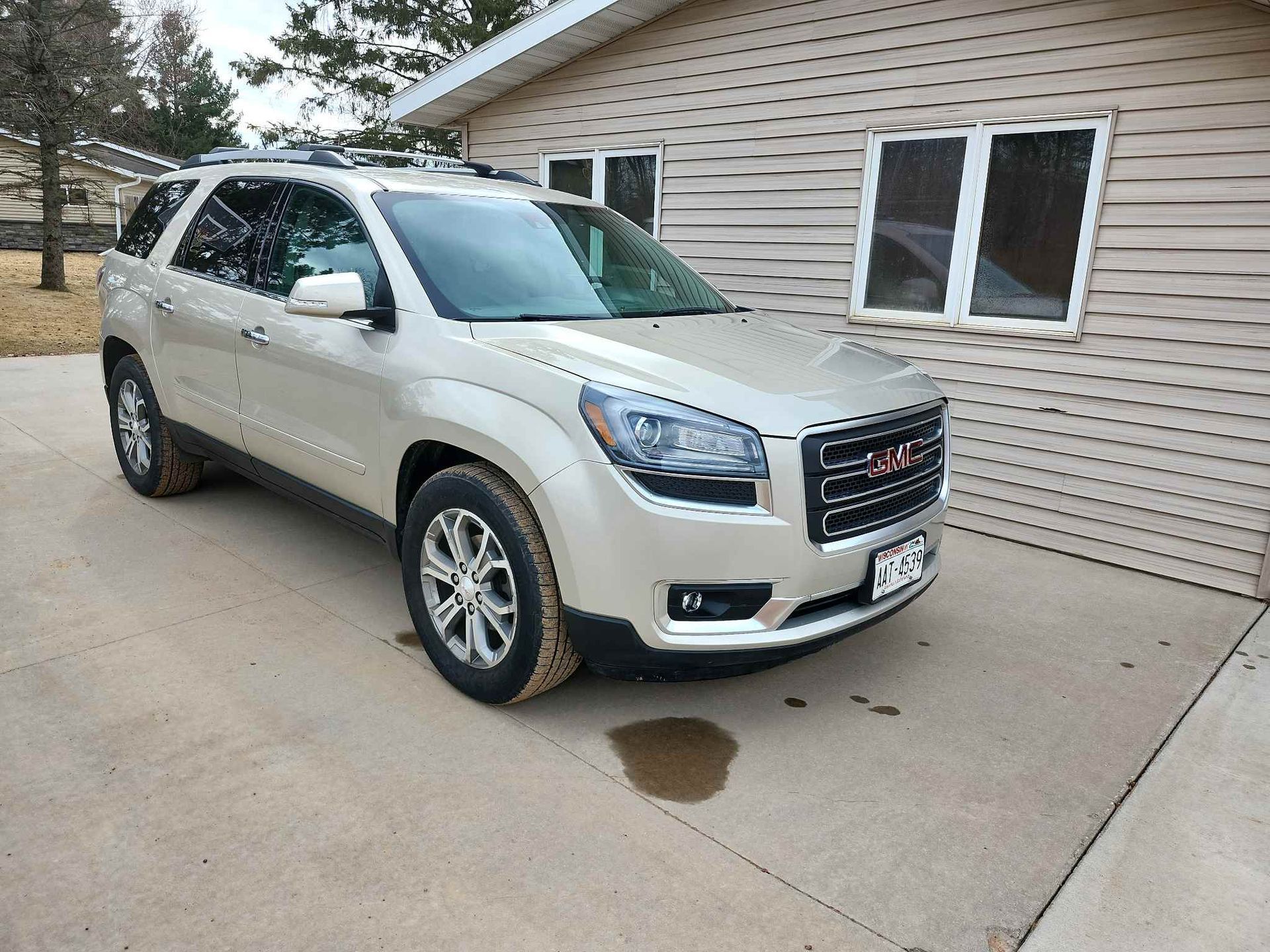 A silver GMC Acadia is parked in a driveway in front of a house.