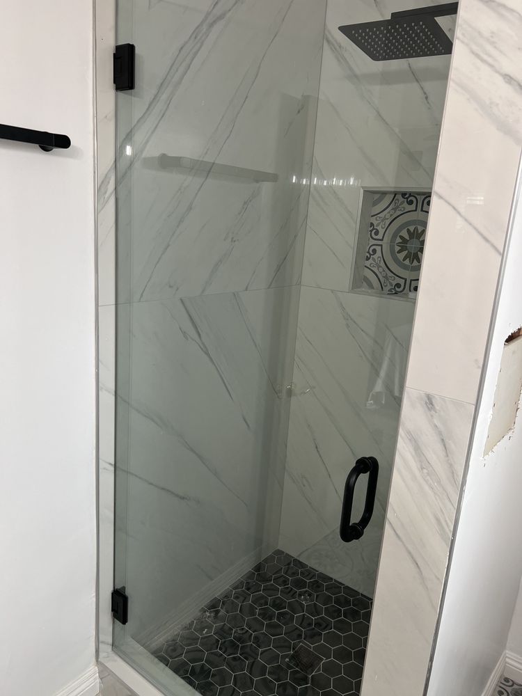A bathroom with a glass shower door and a black handle.