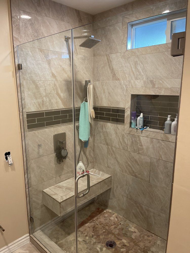 A bathroom with a walk in shower with a glass door and a bench.