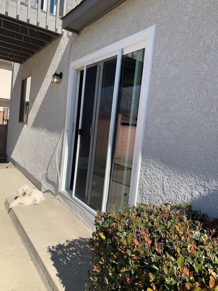 A white dog is sitting on the steps of a house next to a sliding glass door.