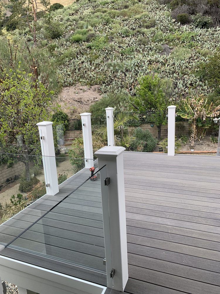 A deck with a glass railing and a view of a forest.