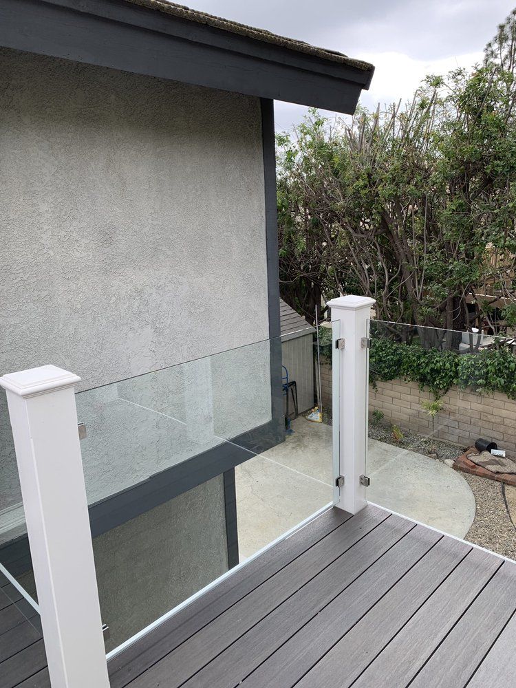 A deck with a glass railing and a fence in front of a house.