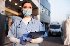 A masked nurse stands outside with a clipboard.