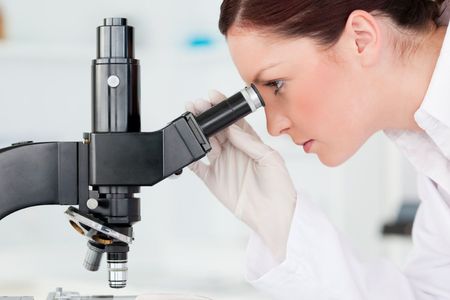 A woman is looking through a microscope in a lab