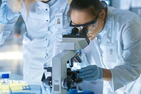 Two female scientists are looking through a microscope in a laboratory.